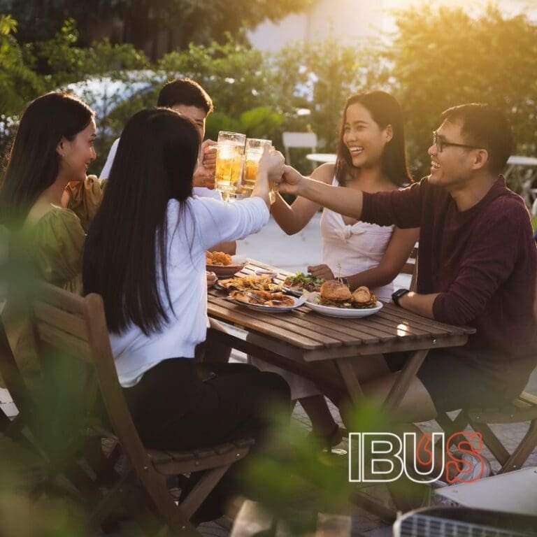 grupo de personas sentadas frente a una mesa al aire libre que sonríen mientras toman cerveza