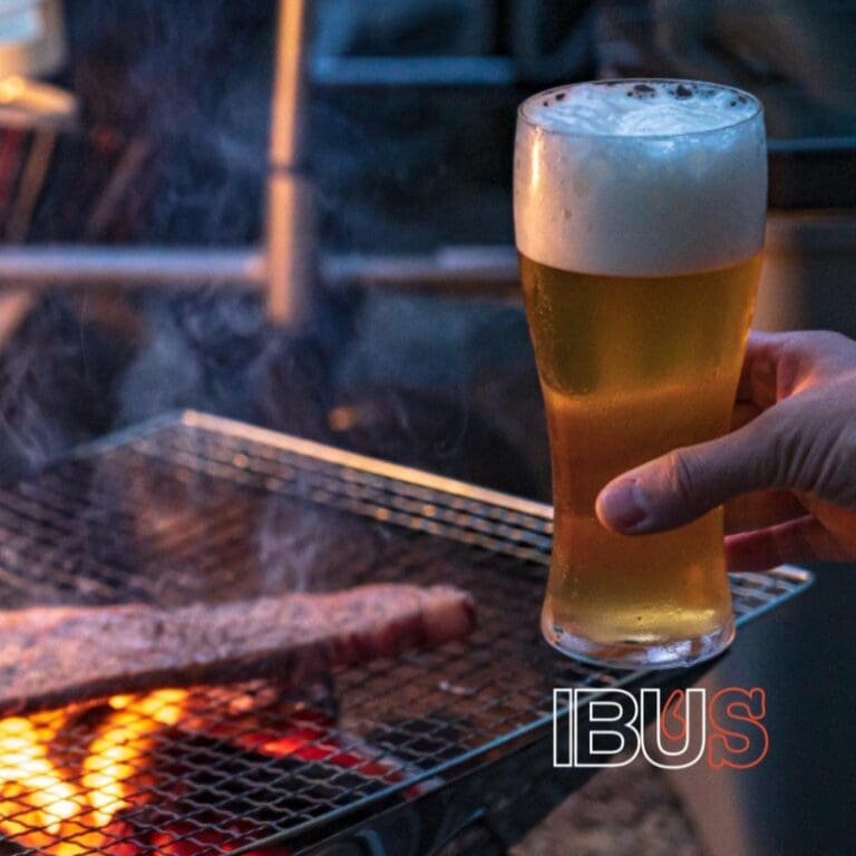 Vaso de cerveza artesanal con espuma, junto a una parrilla con carne en Monterrey.