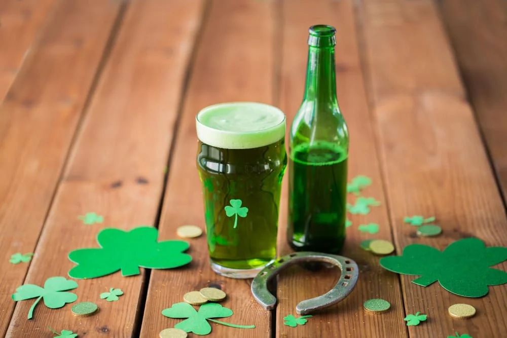 Cerveza verde en vaso y botella con tréboles y herradura para el Día de San Patricio